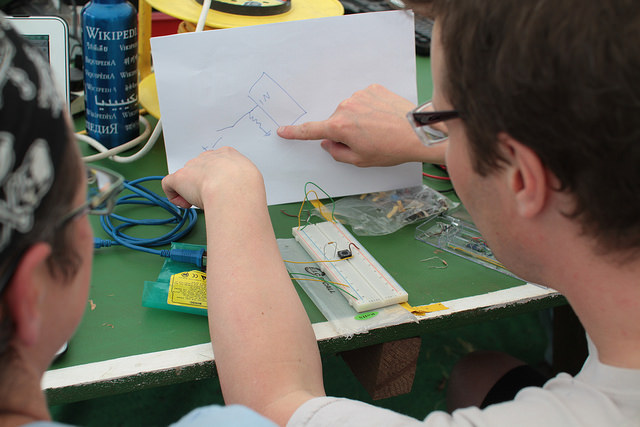 Photo of two people analysing a drawing of an electronic circuit and working with a breadboard